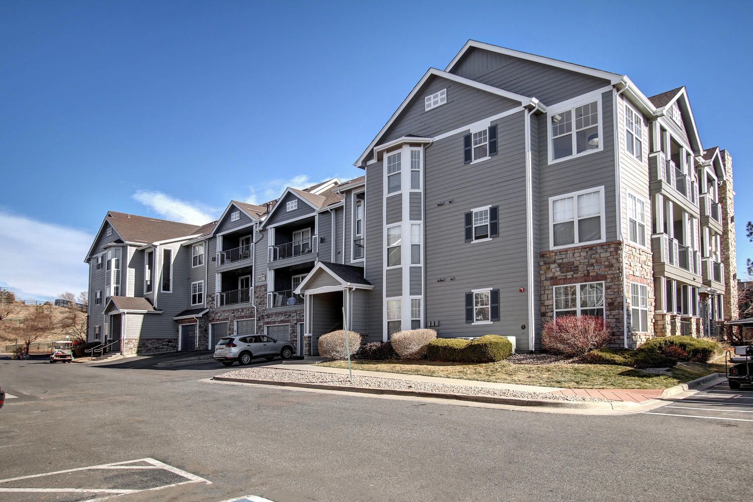 Exterior view of a multi-building apartment complex with gray siding, stone accents, and a parking lot at Briargate on Main apartments in Parker, CO.