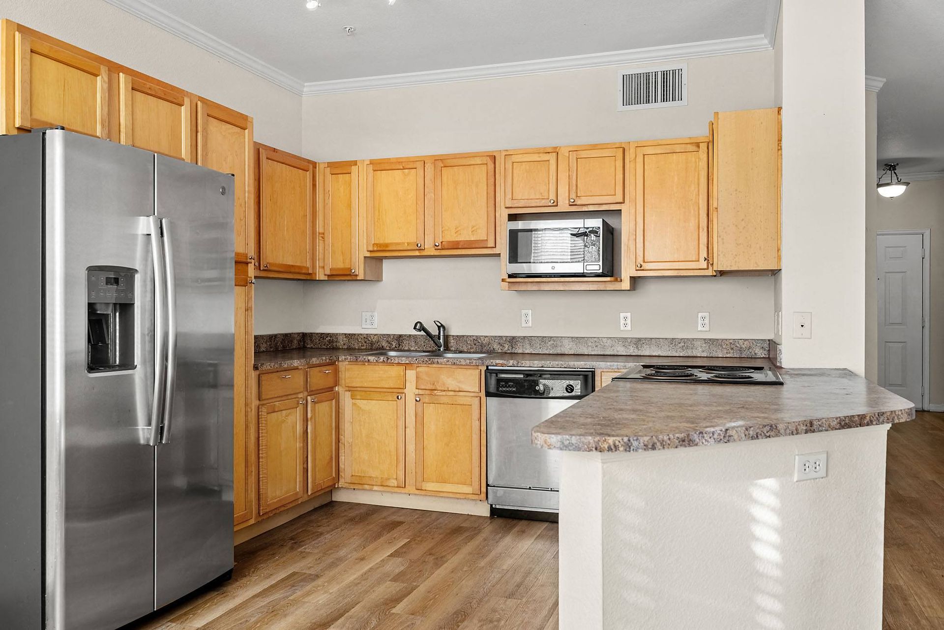 Kitchen in apartment with wood cabinetry, stainless steel refrigerator, microwave, and stove at Briargate on Main apartments in Parker, CO.