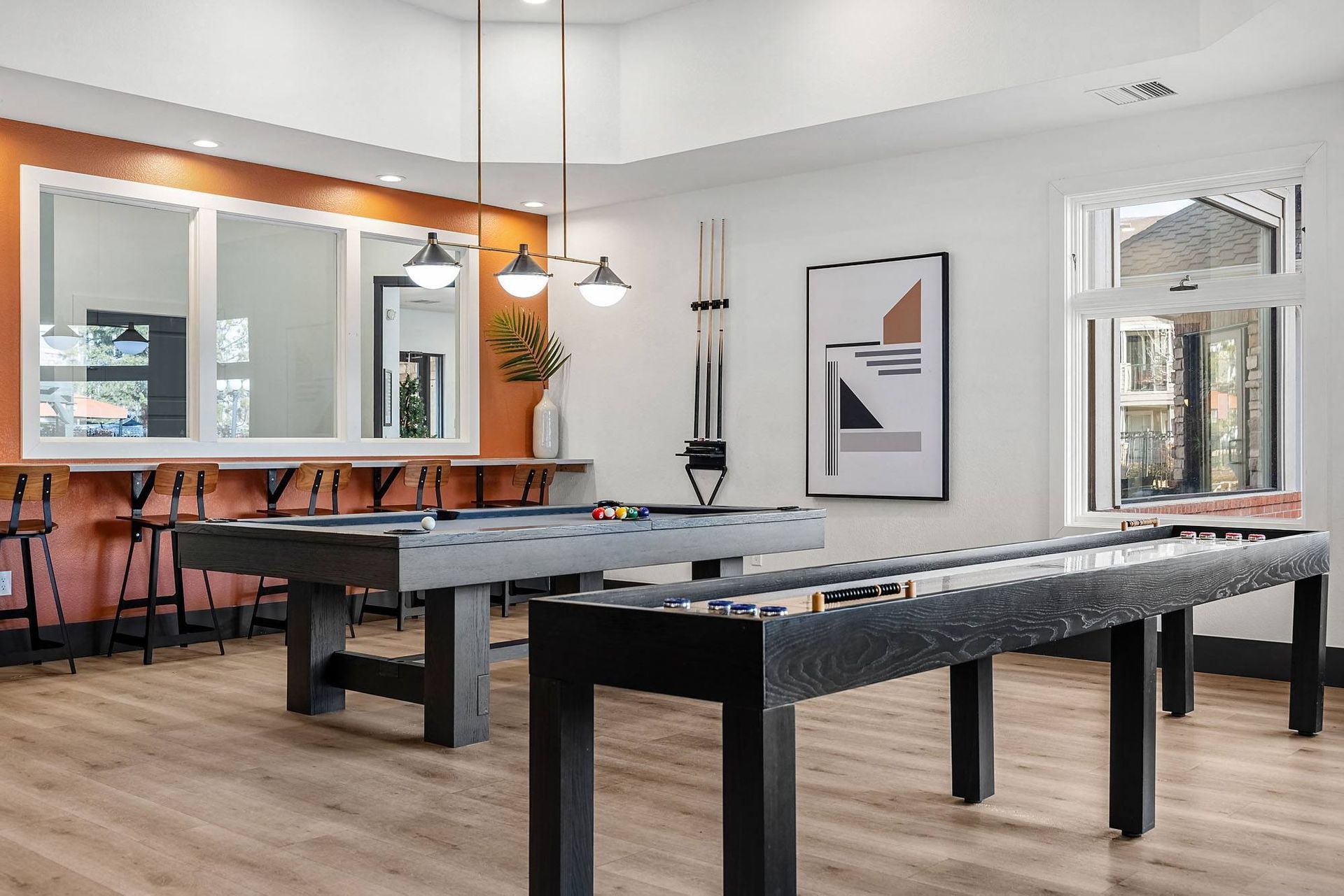 Interior game room with two pool tables, bar seating, warm wood floor, and modern art at Briargate on Main apartments in Parker, CO.