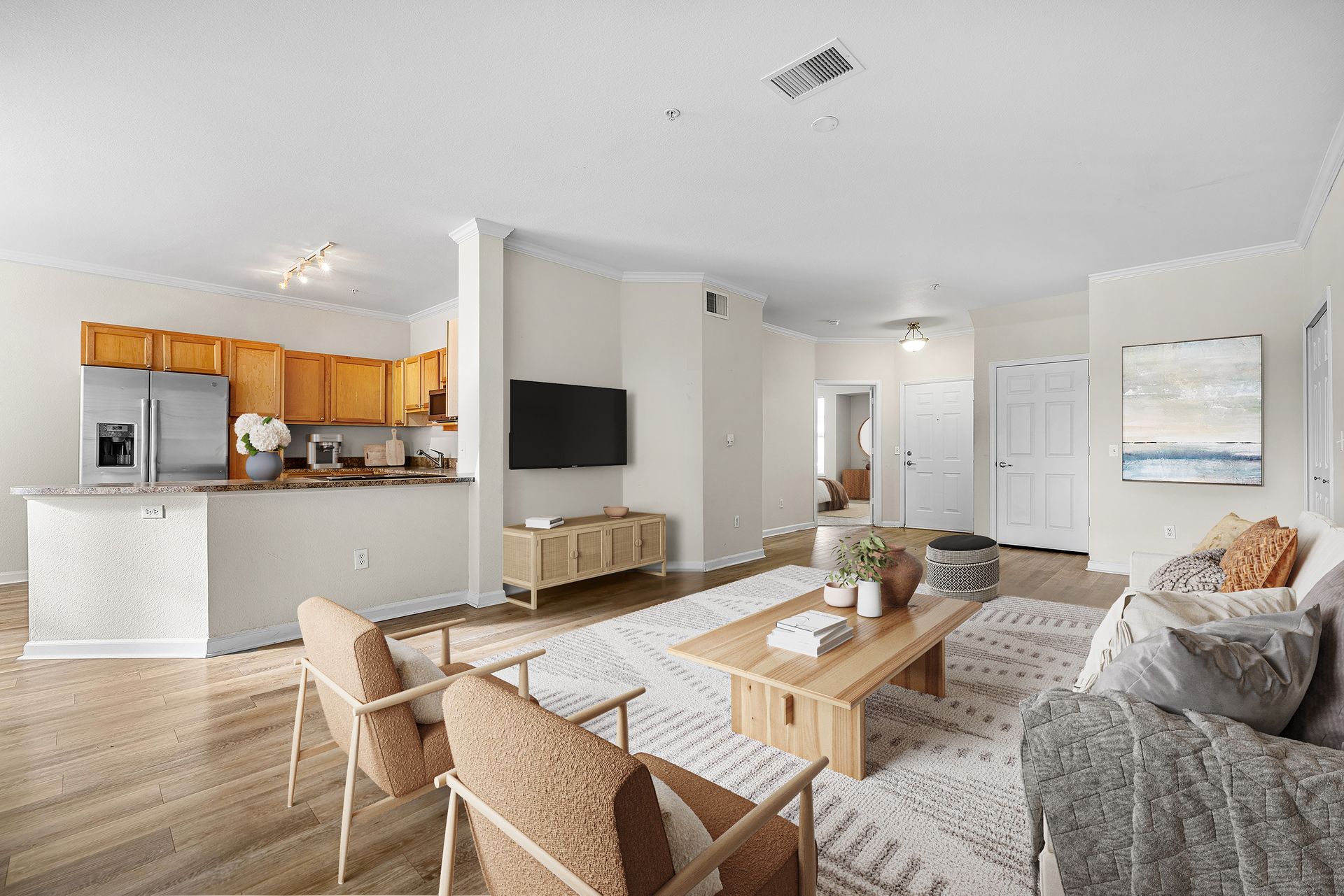 Open-concept living area with kitchen counter, hardwood floors, beige walls, and a wall-mounted TV at Briargate on Main apartments in Parker, CO.