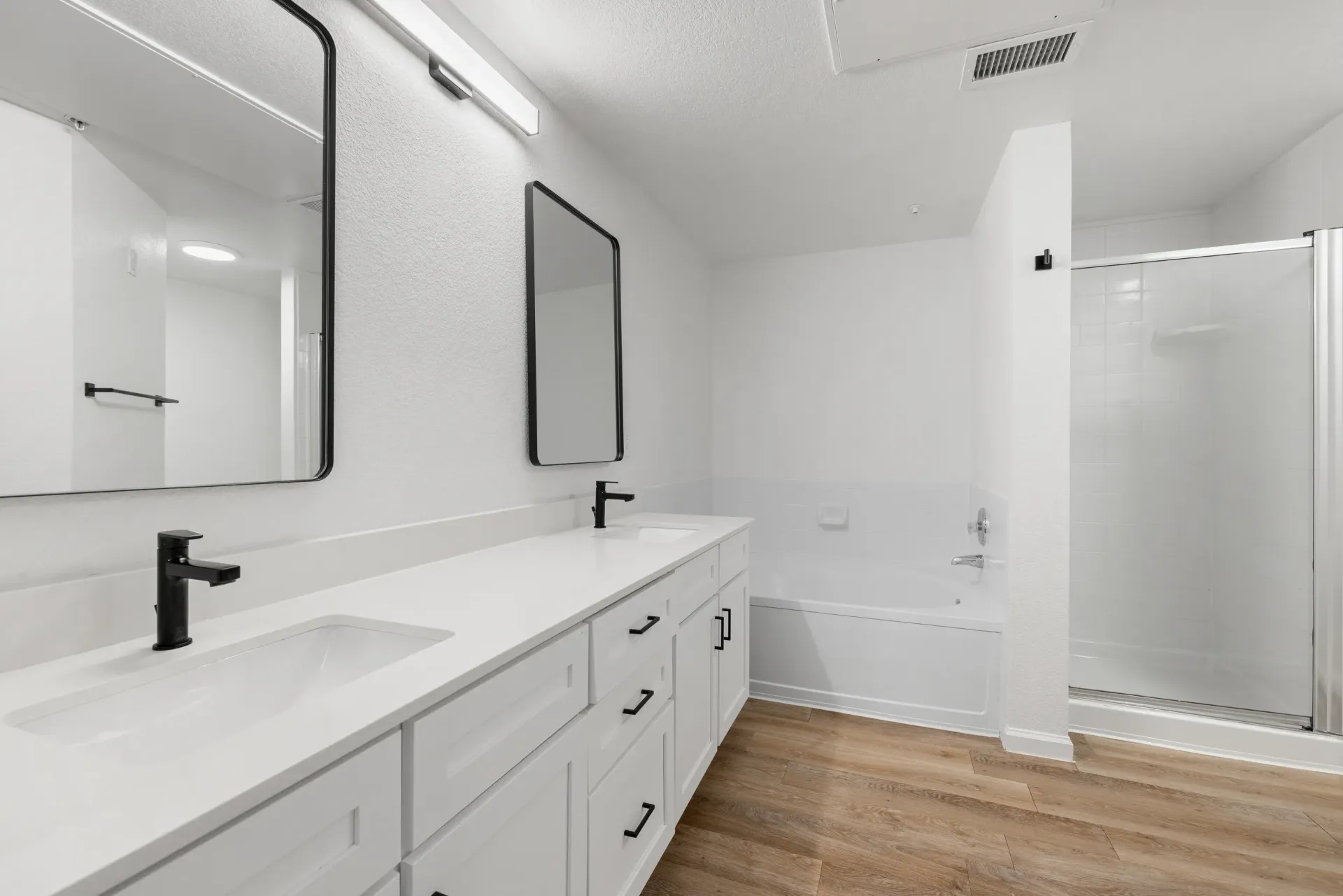 Modern white bathroom with a double-sink vanity and a glass-enclosed shower at Briargate on Main apartments in Parker, CO.