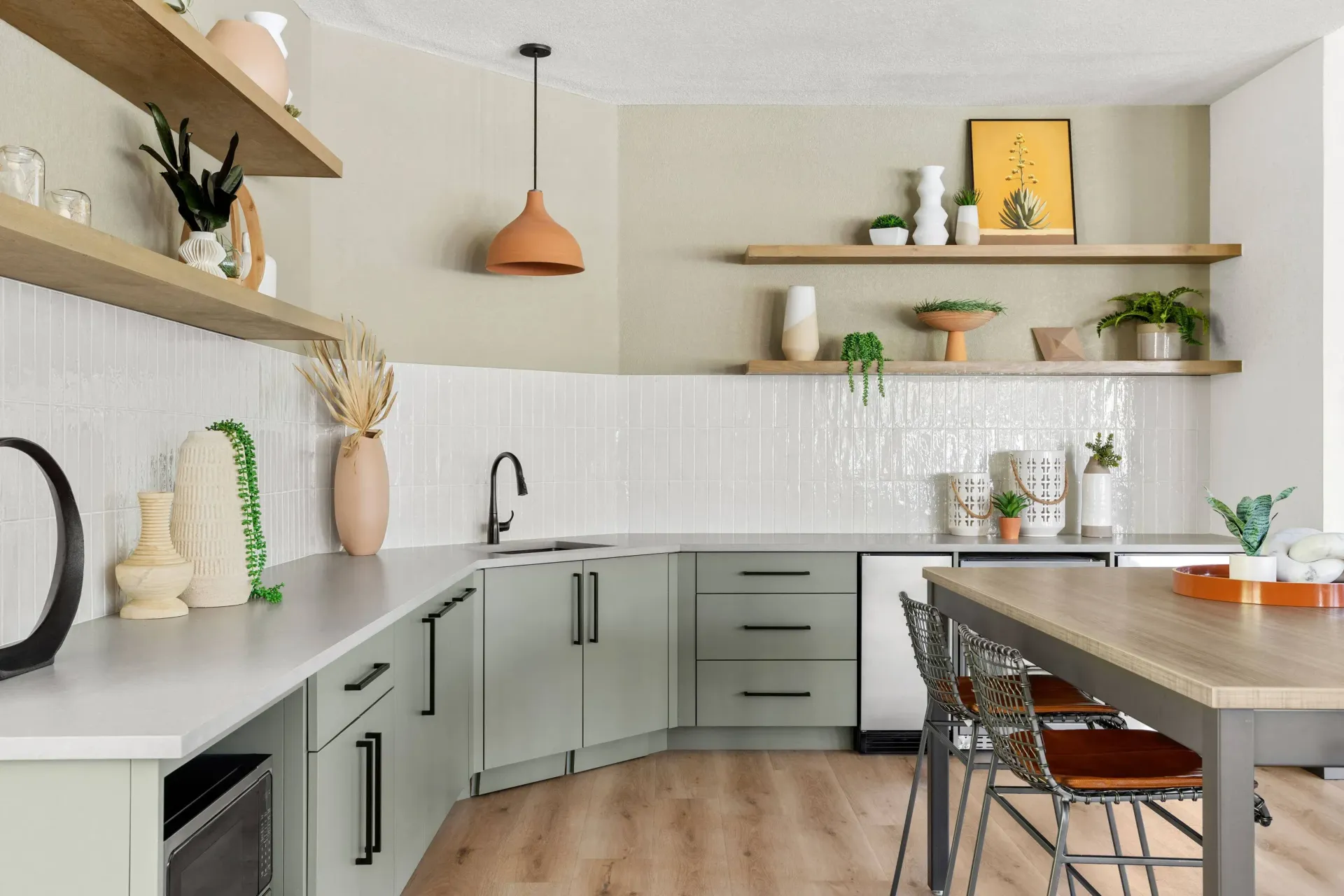 Modern apartment kitchen with light-green cabinets, white tile backsplash, open wood shelves, and island at Briargate on Main apartments in Parker, CO.