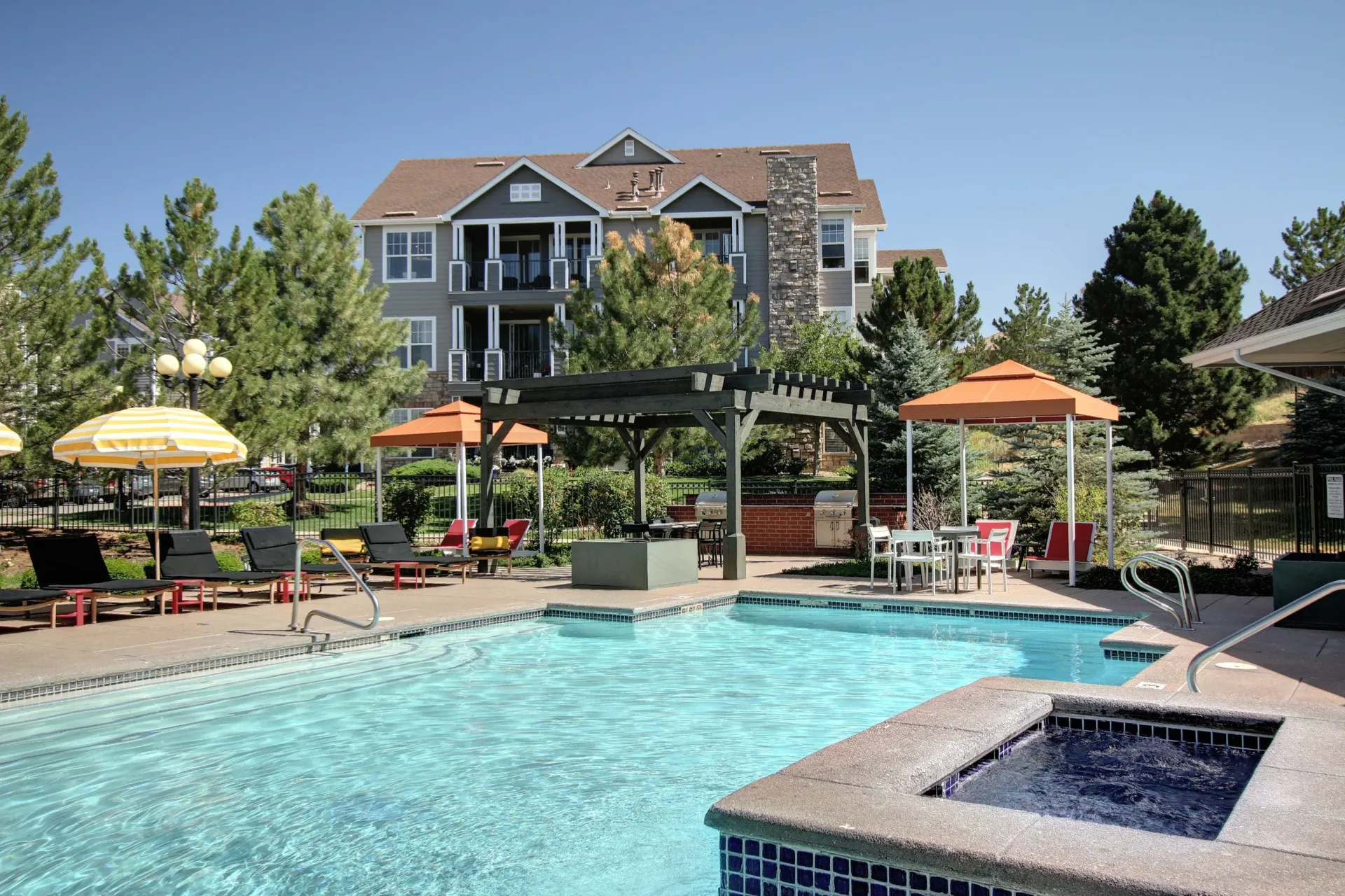 Outdoor pool area with lounge chairs, umbrellas, and a pergola at a residential community at Briargate on Main apartments in Parker, CO.