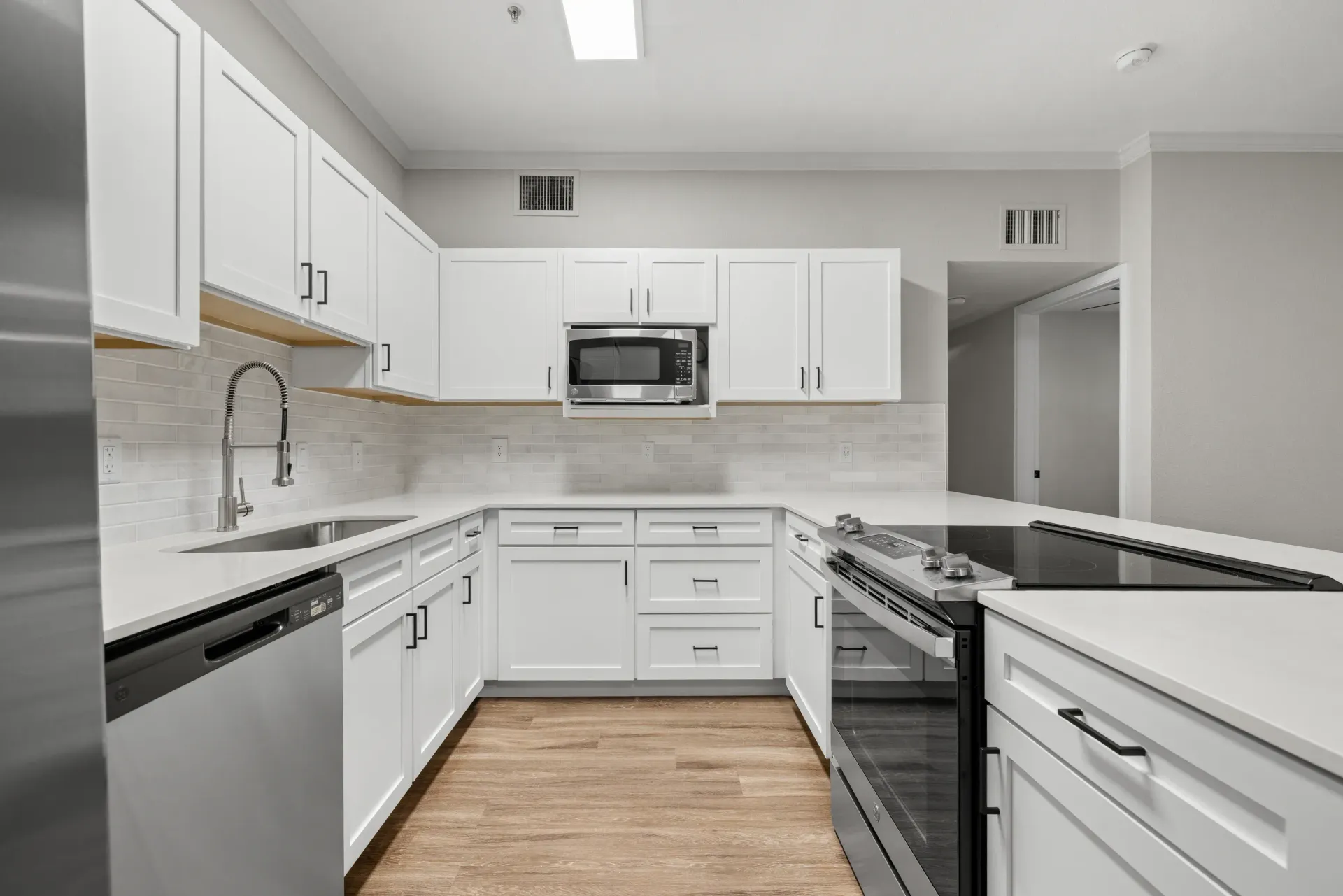Modern apartment kitchen with white cabinets, stainless steel appliances, and a tile backsplash at Briargate on Main apartments in Parker, CO.