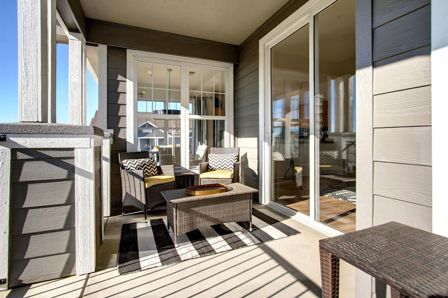 Outdoor apartment balcony with wicker chairs, a coffee table, and a striped rug near sliding glass doors at Briargate on Main apartments in Parker, CO.