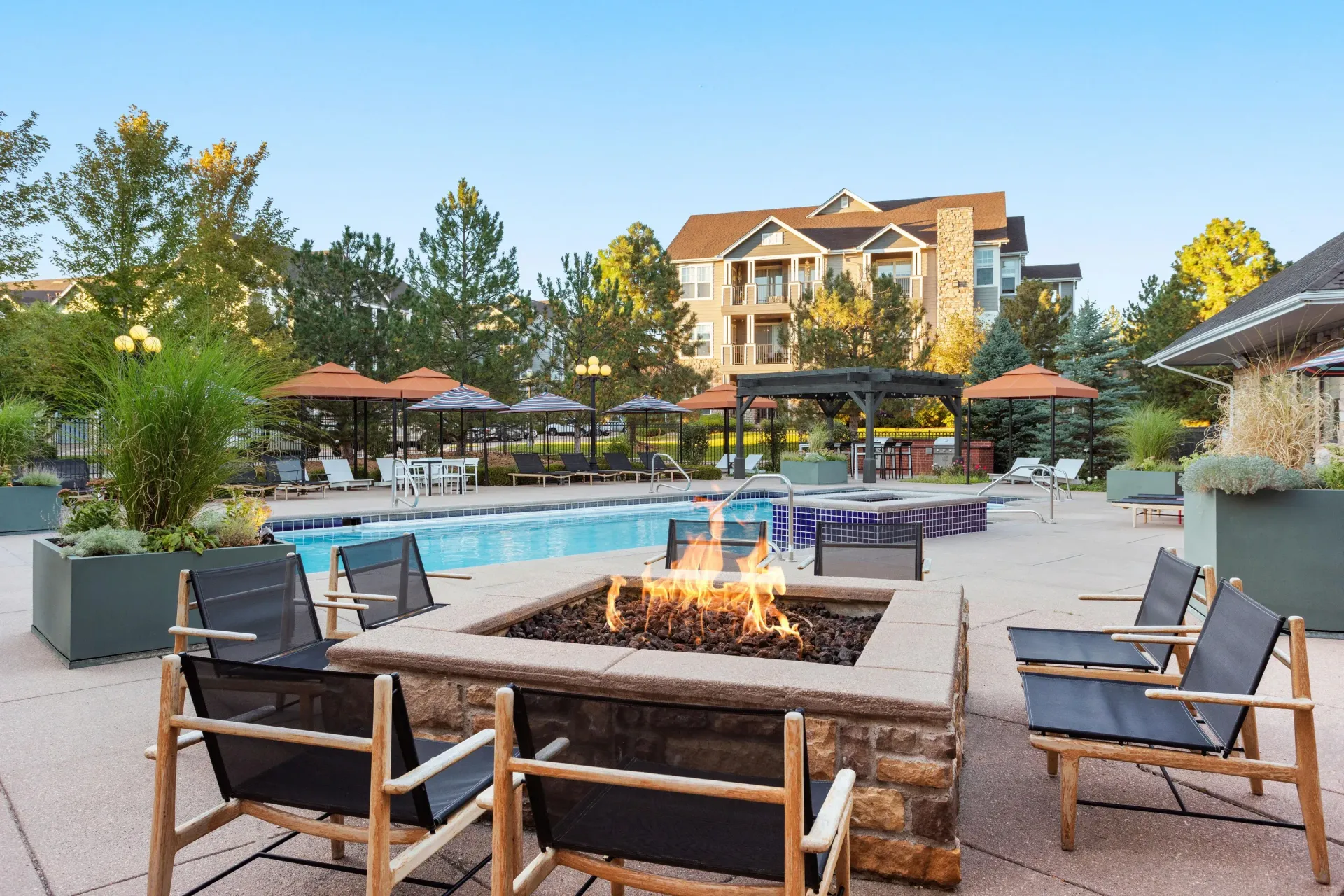 Outdoor apartment community pool area with lounge chairs, umbrellas, and a fire pit at Briargate on Main apartments in Parker, CO.