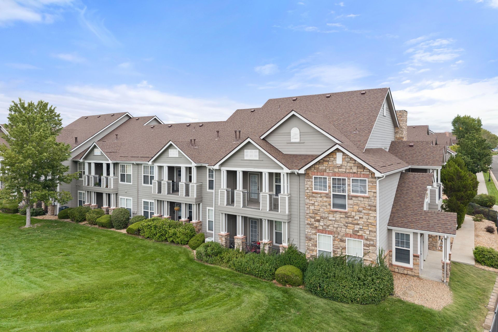 Row of modern apartments with balconies and brown roofs beside a green lawn