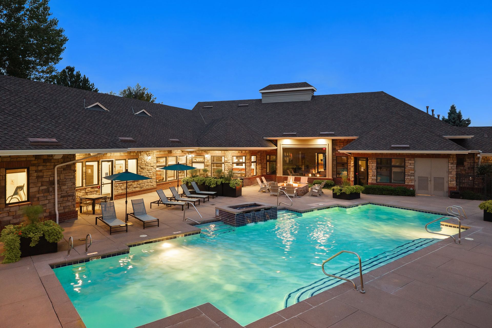 Pool patio with lit swimming pool, lounge chairs, and the leasing office