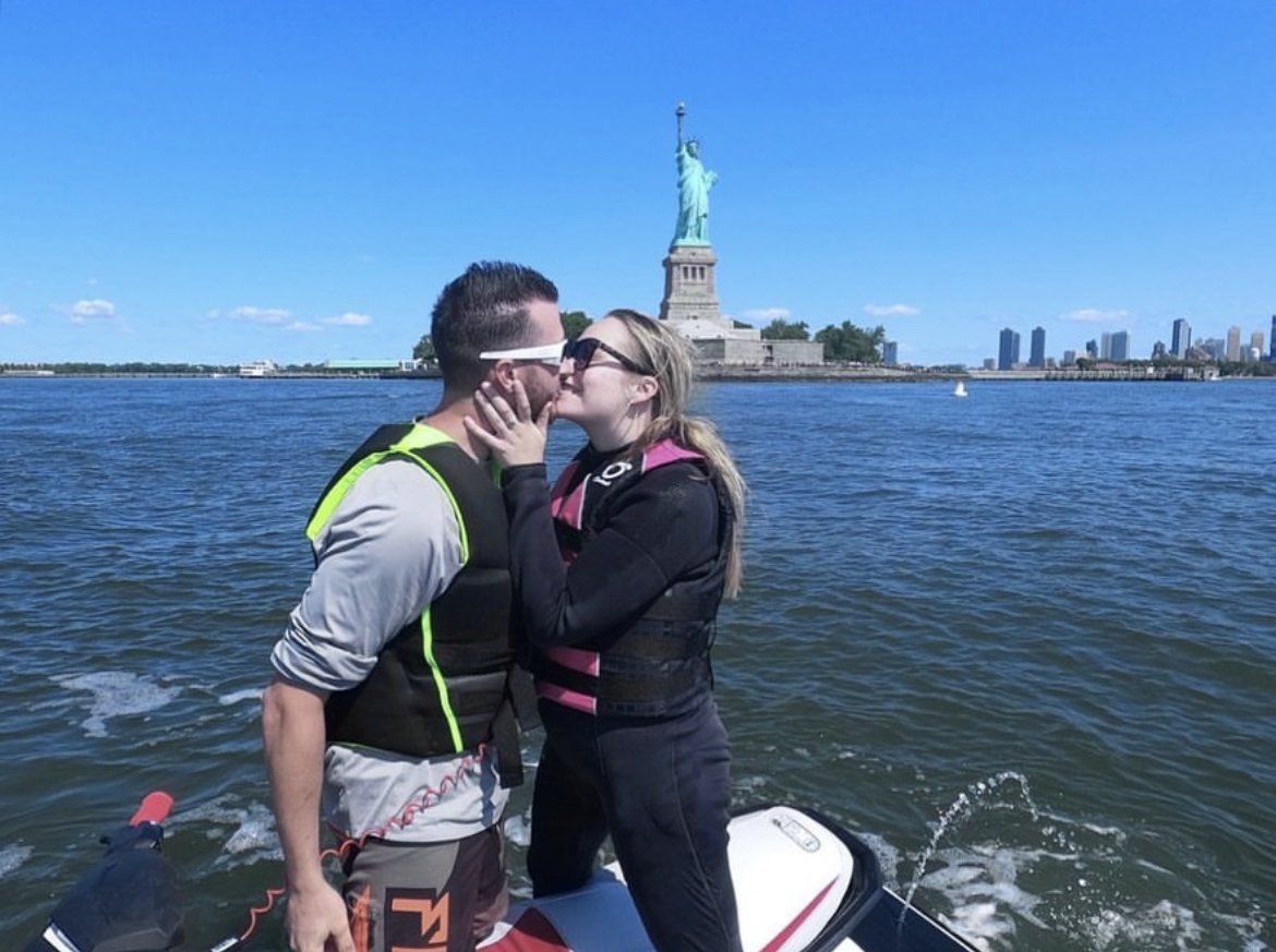 couple kissing on jet ski in front of statue of liberty