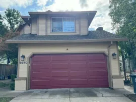 Two-story house with beige siding and a maroon garage door under a cloudy sky