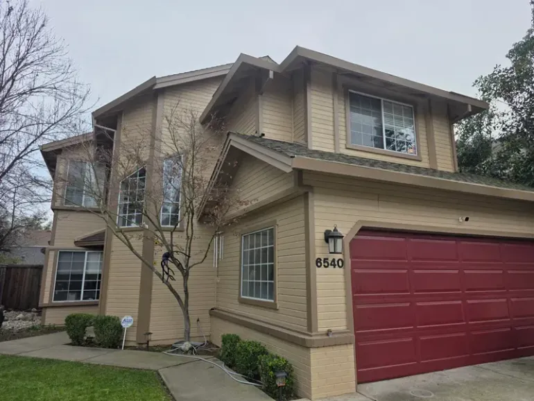 Suburban two-story tan house with red garage door and front windows