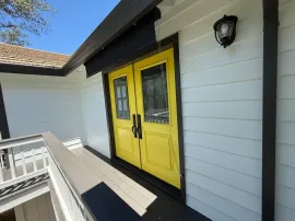Bright yellow double doors on a white exterior wall with a porch railing and wall lantern.