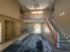 Empty living room under renovation with plastic-covered floor and staircase to loft.