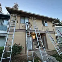Two-story apartment exterior with five ladders leaning against the building during maintenance