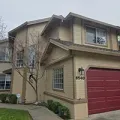 Two-story beige house with red garage door and small front tree