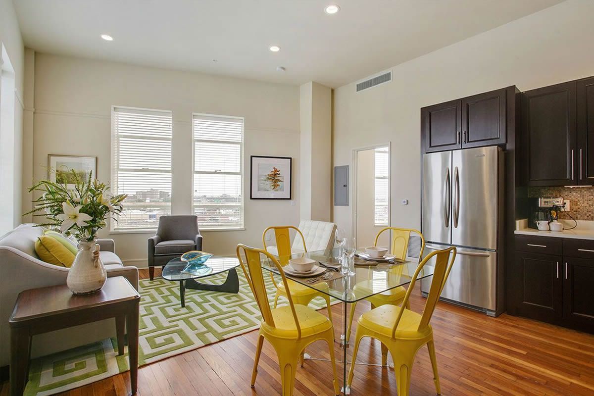 A living room with a dining table and chairs and a stainless steel refrigerator.