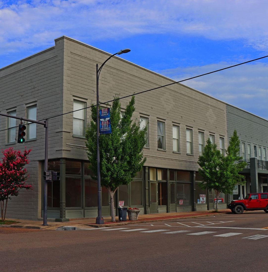 A red car is parked in front of a building with a sign that says ' nc ' on it