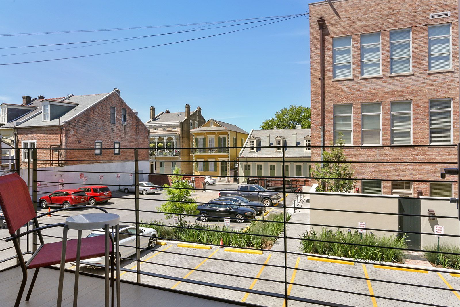 A balcony with a view of a parking lot and a brick building.