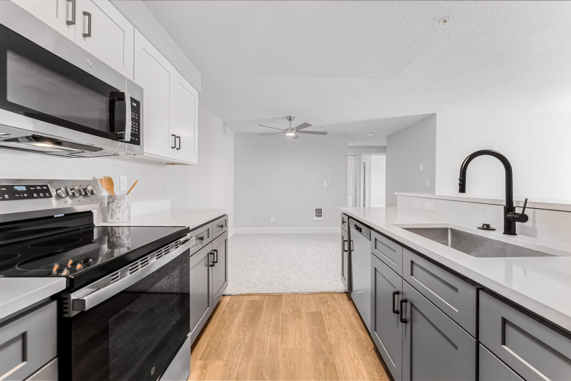 Modern apartment kitchen with white countertops, gray cabinets, and stainless steel appliances.