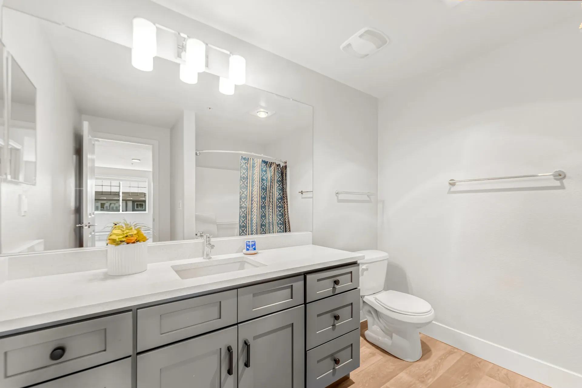Contemporary apartment bathroom with gray vanity, large mirror, toilet, and blue patterned shower curtain.