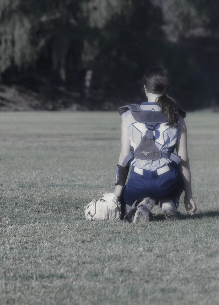 Woman kneeling on a grassy field, wearing protective gear, with a ball nearby.