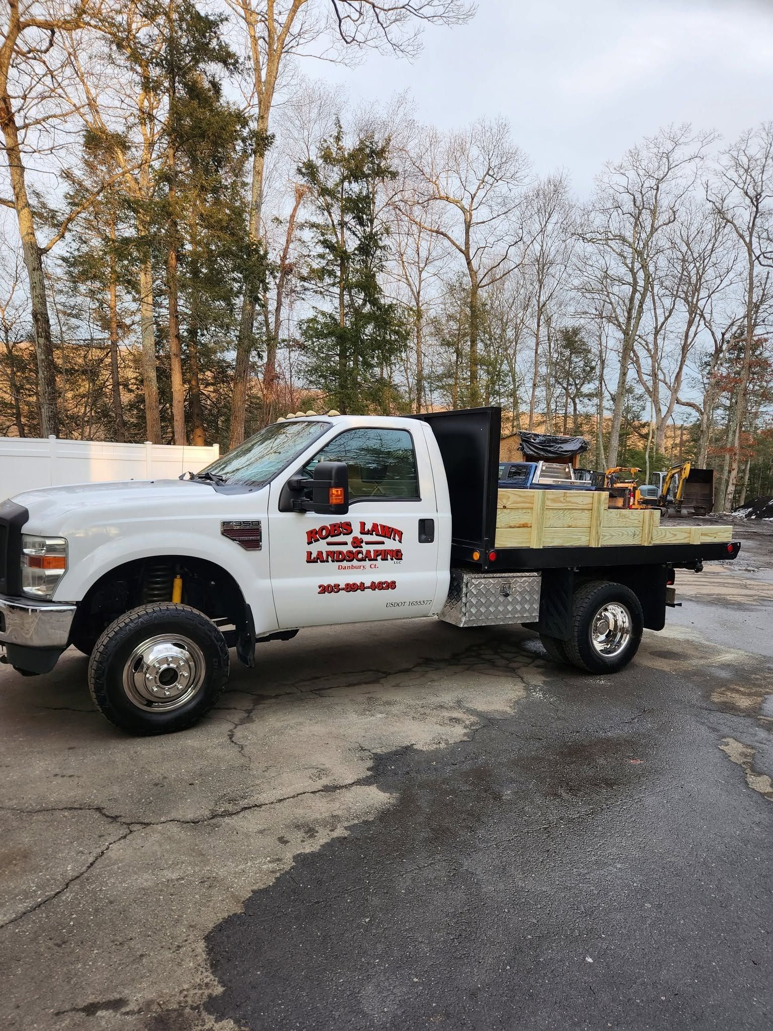 White utility pickup truck with company logo parked on a wet lot near trees and other work vehicles