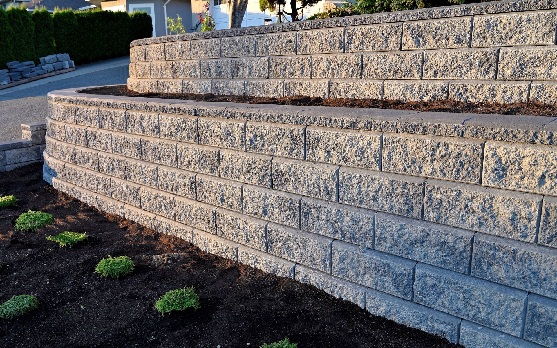 Stone retaining wall with terraced steps beside a landscaped slope and dark soil groundcover