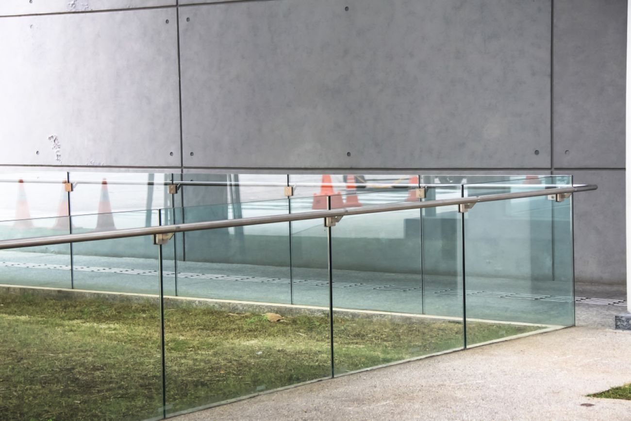 A Glass Fence Surrounds a Grassy Area in Front of a Building — Top Shelf Glass Pool Fencing & Balustrading in Helensvale, QLD