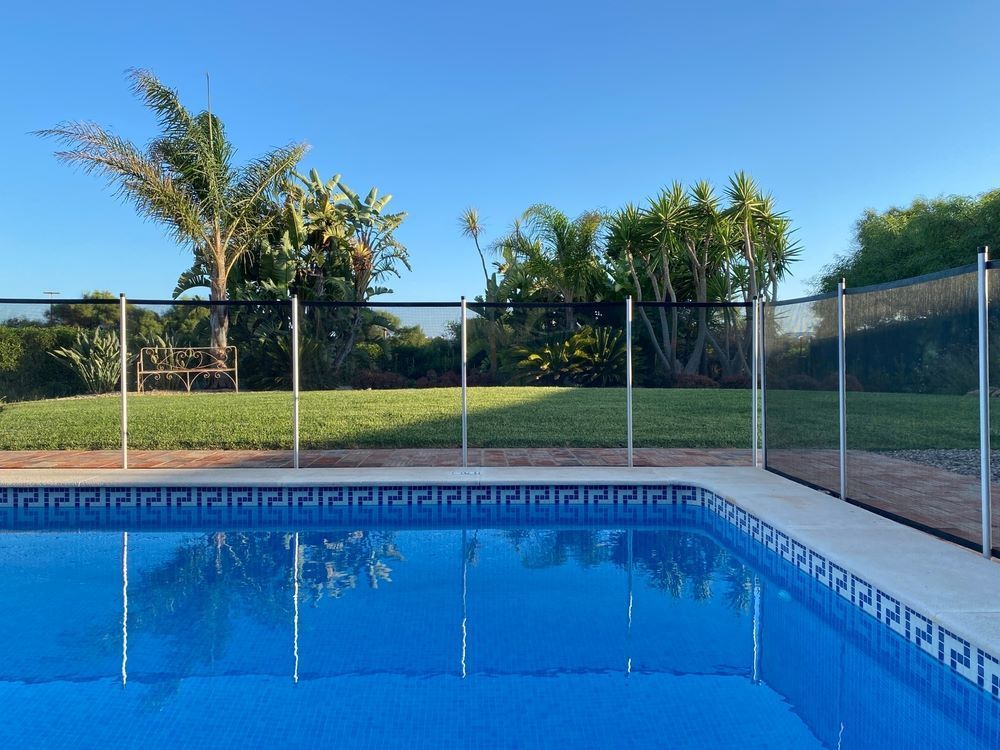 A Swimming Pool With a Glass Fence Around by Trees and Grass — Top Shelf Glass Pool Fencing & Balustrading in Helensvale, QLD