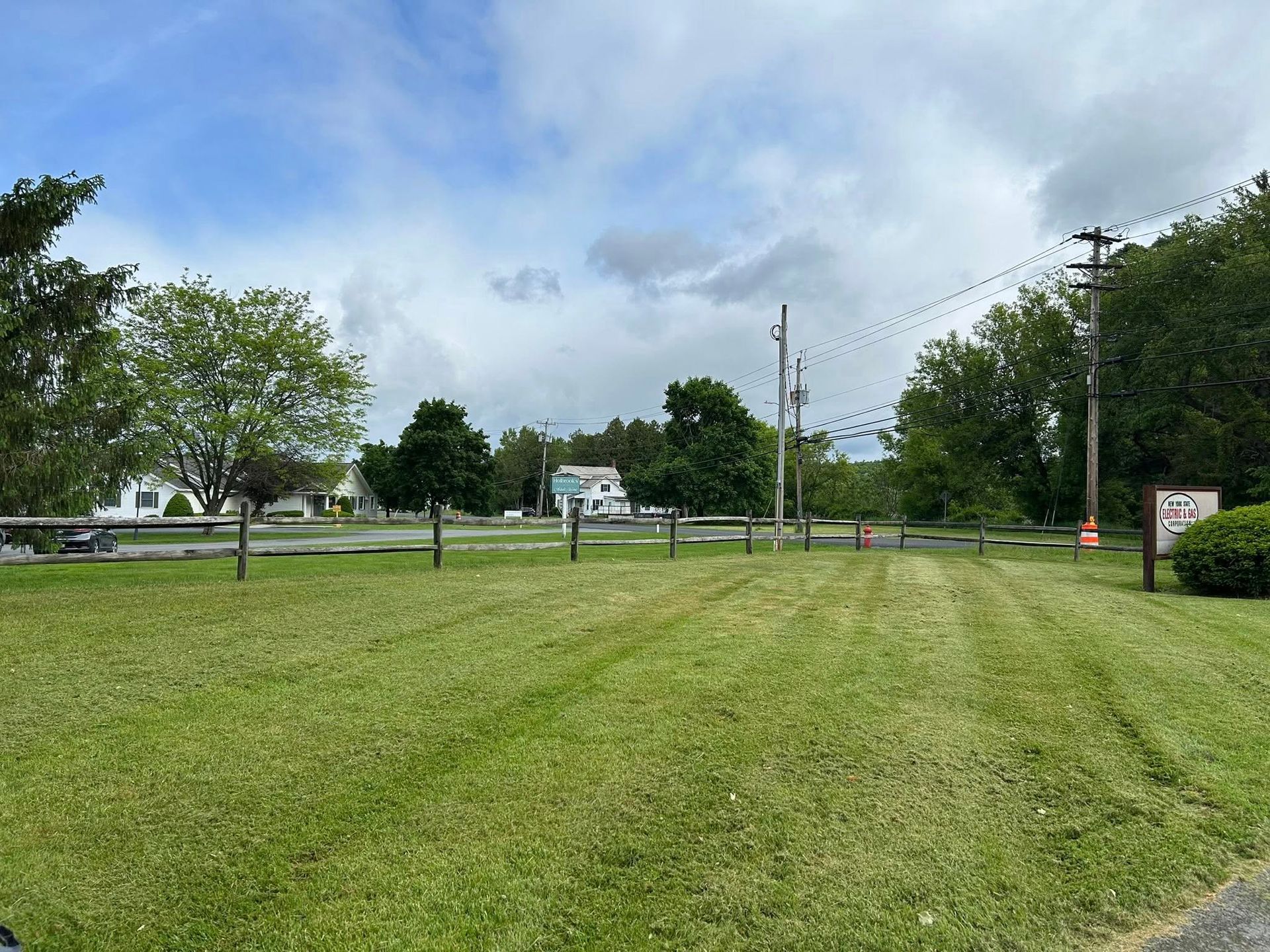 Grassy field beside a road with trees, utility poles, and a cloudy blue sky