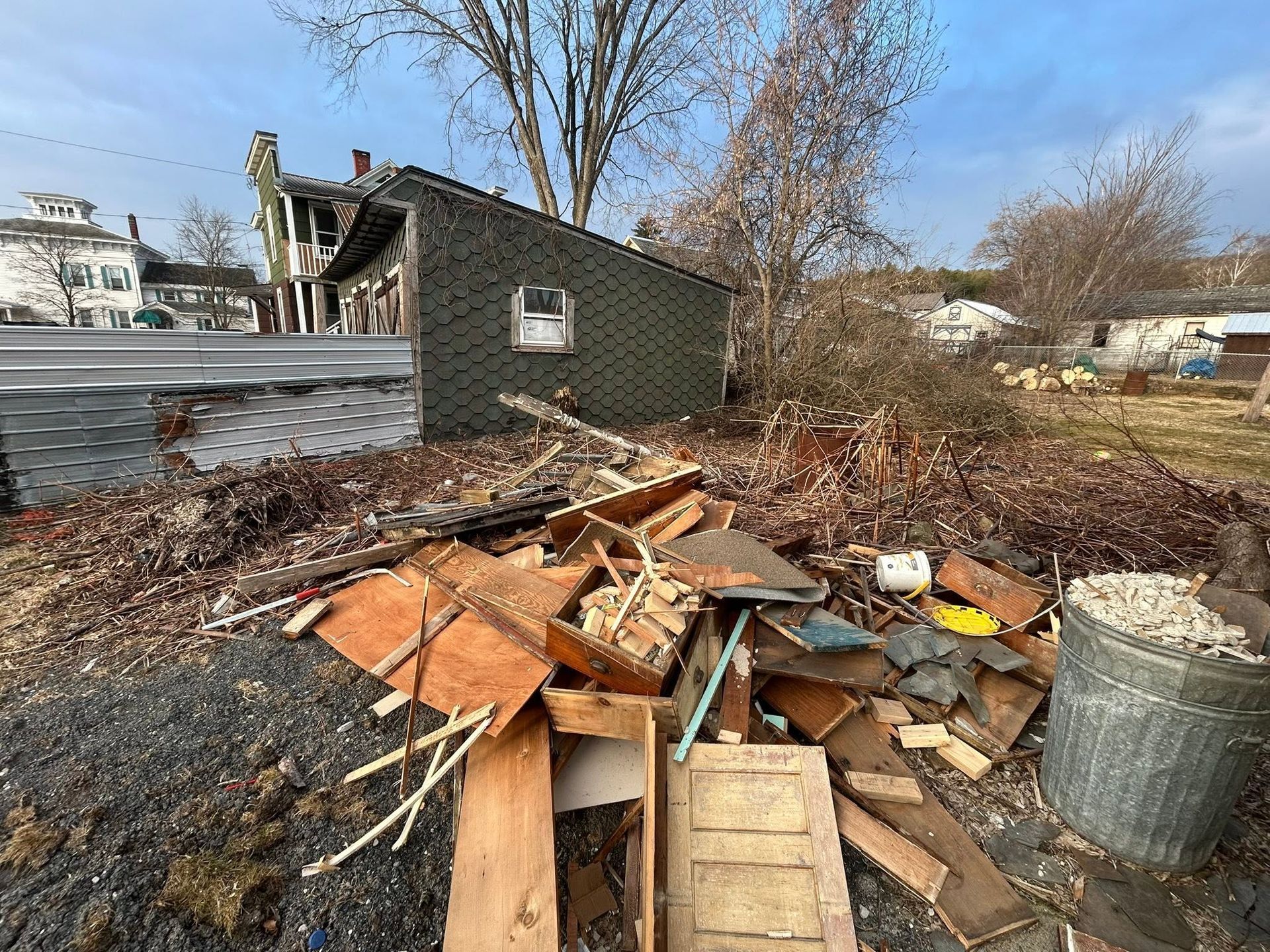 Pile of broken wood and debris in a yard beside a small dark shed on a sunny day.