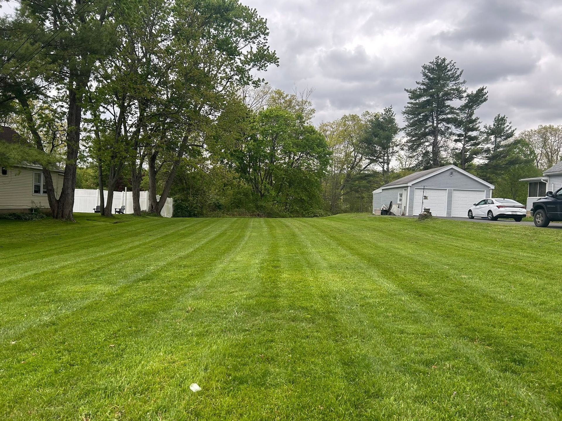 Grassy backyard with trees, a white garage, and cloudy sky
