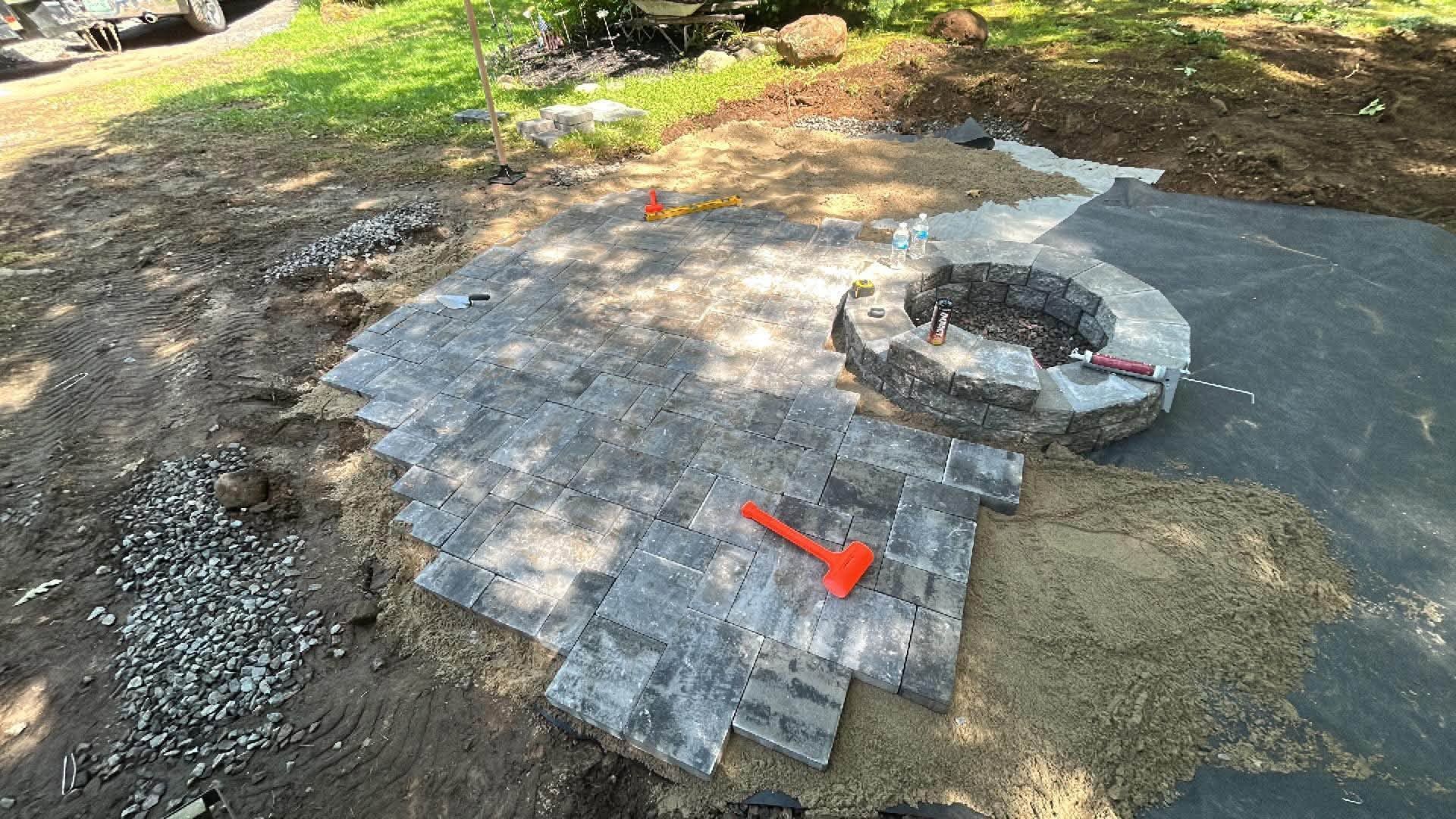 Stone fire pit patio under construction with pavers laid in a curved pattern on a grassy yard