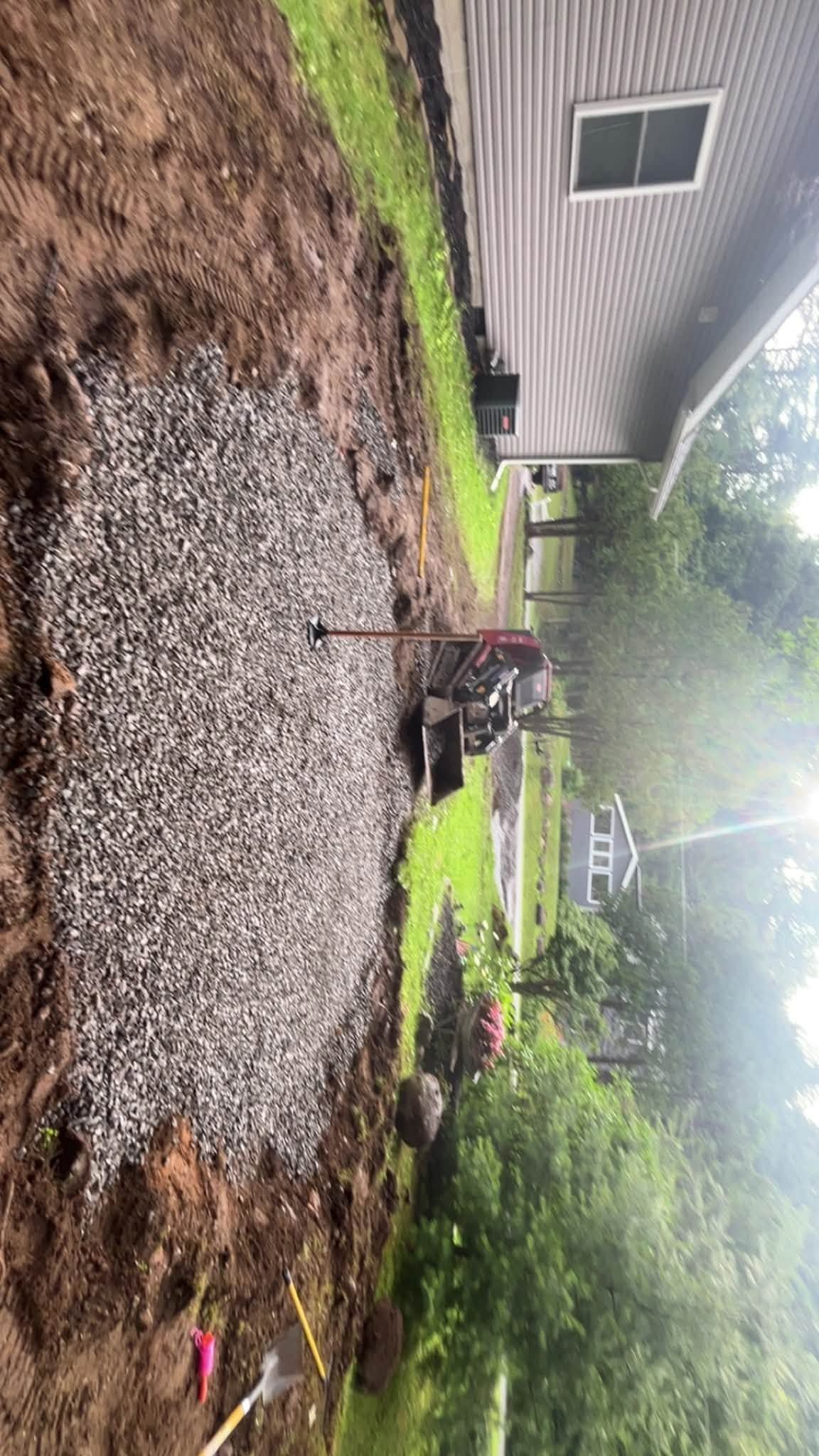 Outdoor gravel yard beside a house with a muddy fire pit, green lawn, and trees in the background