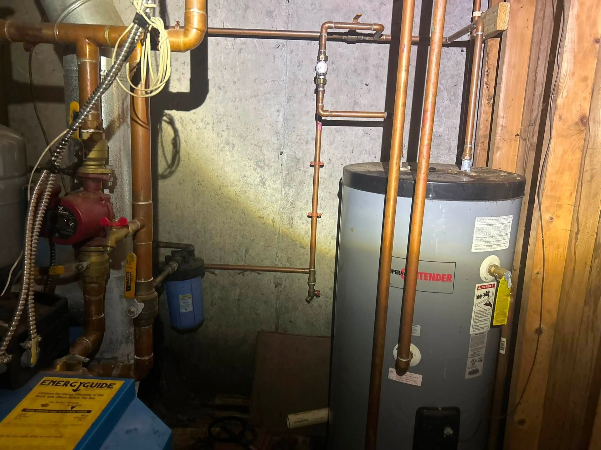 Basement utility room with water heater, pipes, valves, and boiler equipment along a wall.