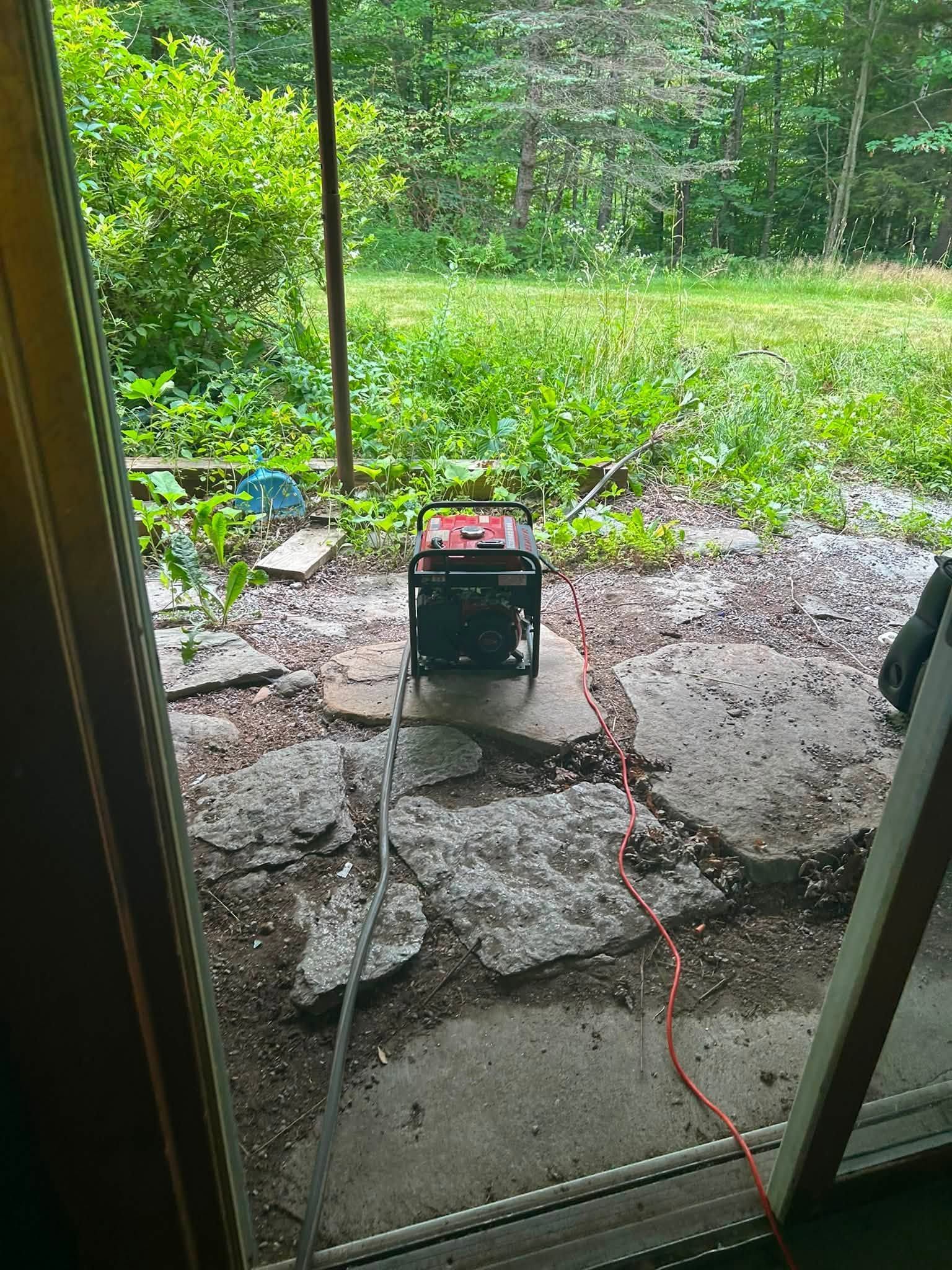 Portable generator on a wet patio outside a doorway, with an orange cord and rain-soaked yard beyond.