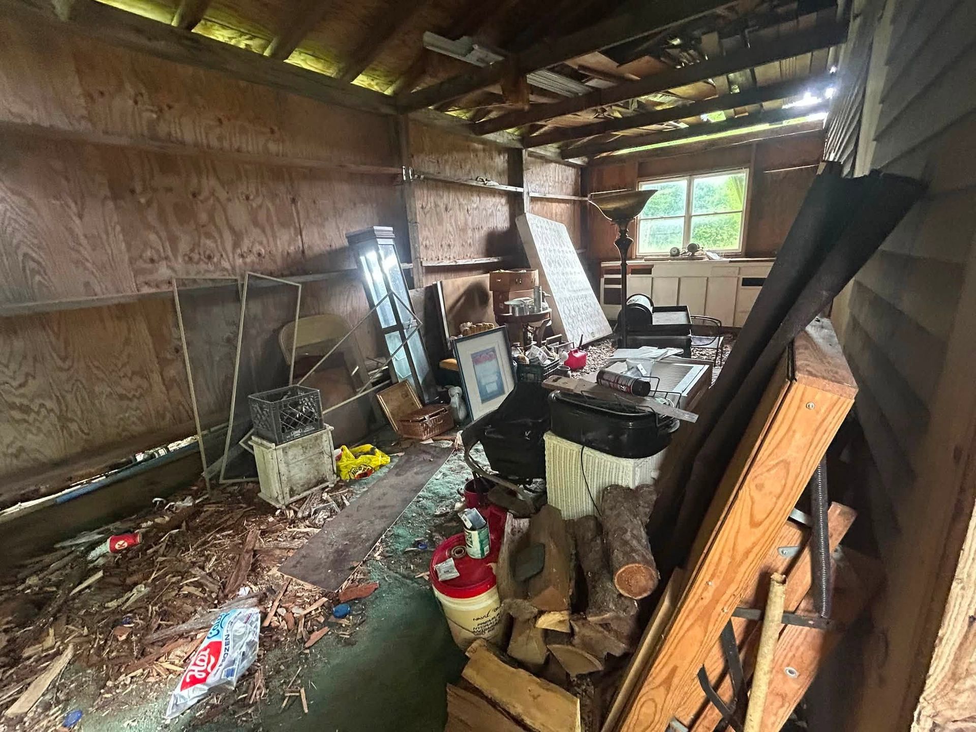 Cluttered, damaged interior with debris, broken items, and exposed wooden walls and roof.