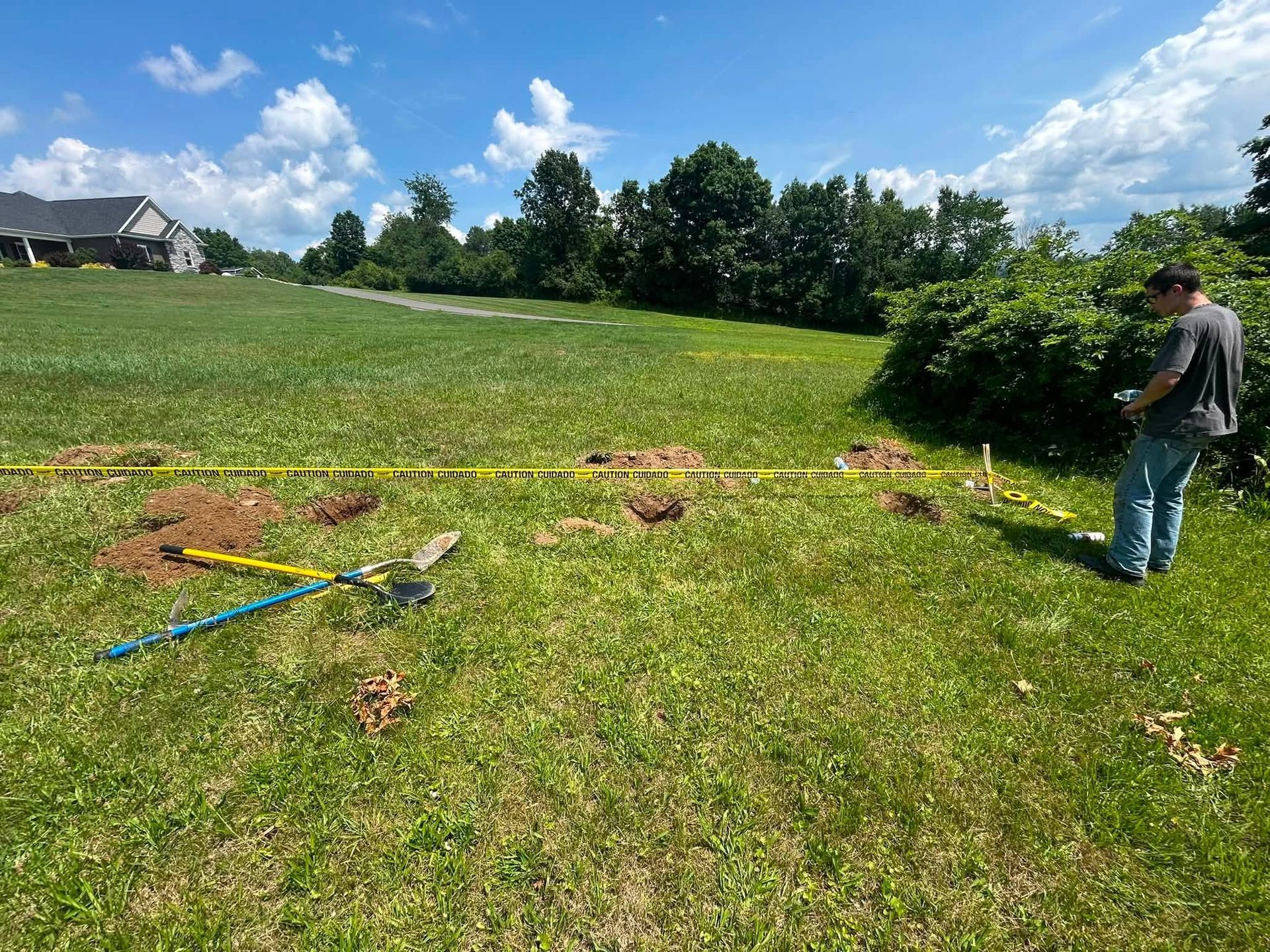 Person standing in a grassy field near scattered tools under a bright blue sky