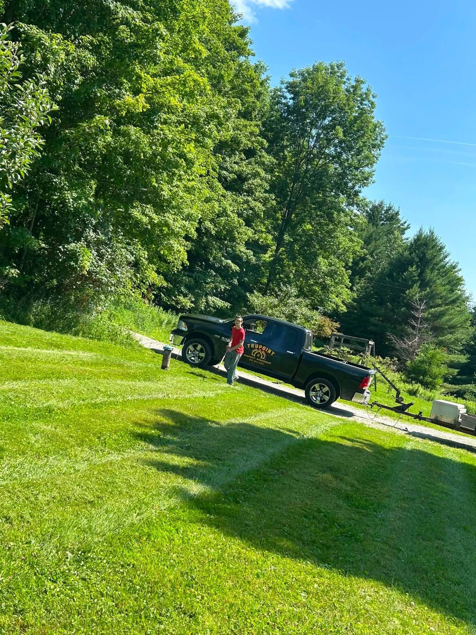 Black pickup truck and person in red shirt on a sunny grassy lawn with trees in the background
