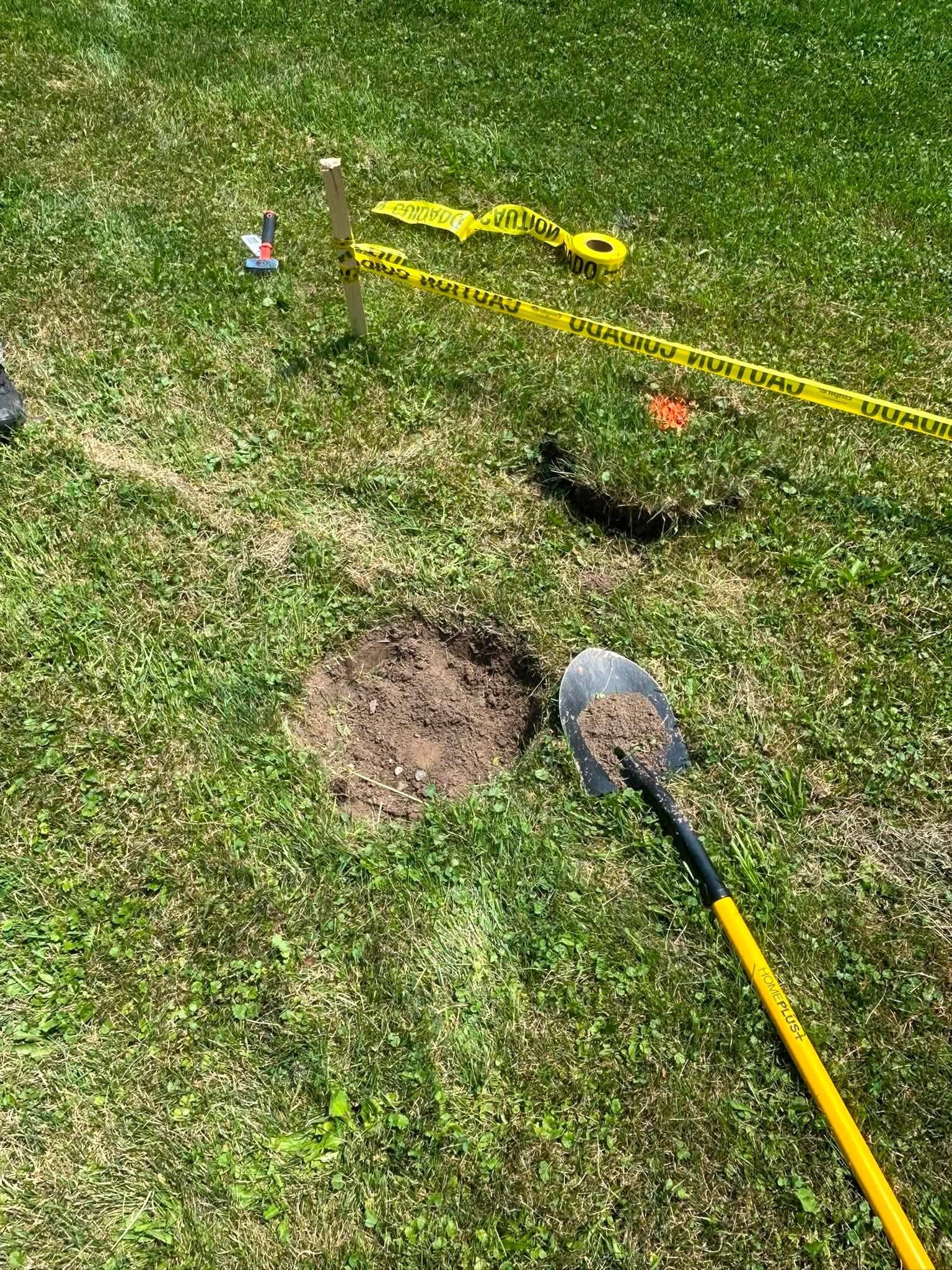Garden lawn with a metal detector and digging tools beside a fresh soil patch and yellow caution tape