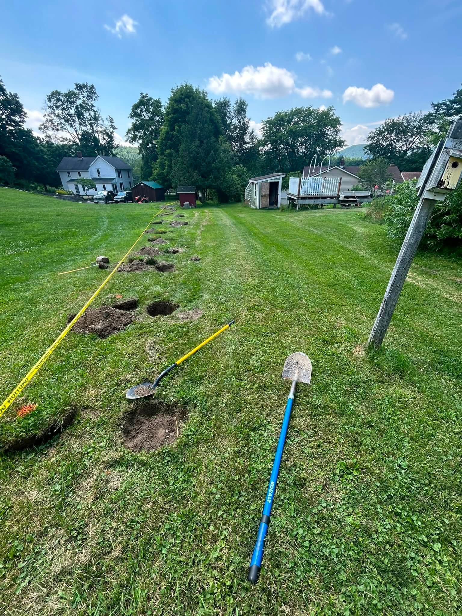 Lawn with marked dig spots and shovels, likely utility work in a grassy yard near homes.