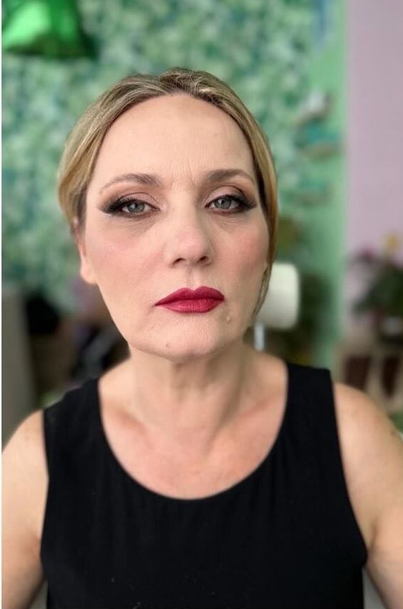Una donna che indossa una canottiera nera e un rossetto rosso guarda la telecamera.