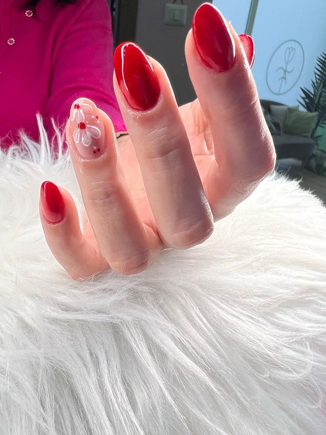 La mano di una donna con le unghie rosse è seduta su una coperta bianca di pelliccia.