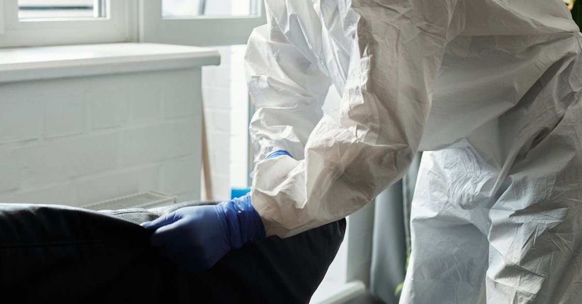A person in a protective suit is cleaning a chair with a spray bottle.