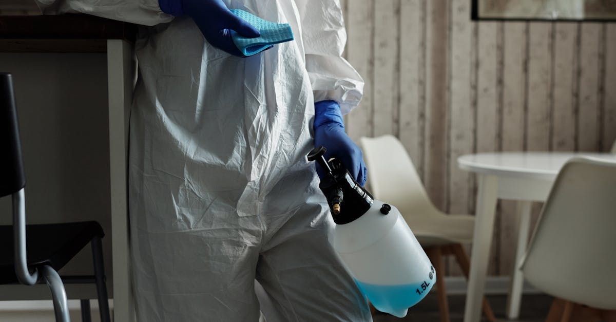 A person in a protective suit is cleaning a room with a spray bottle.