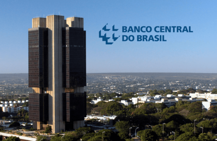Edifício do Banco Central do Brasil com o logotipo da instituição ao fundo, em contraste com a paisagem urbana.