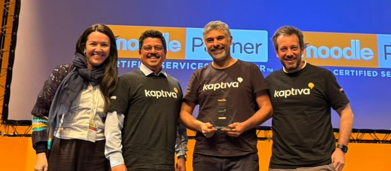 Quatro pessoas segurando um troféu no palco com uma placa de “Parceiro das Américas”. Elas estão vestindo camisetas da “kaptiva” e sorrindo.