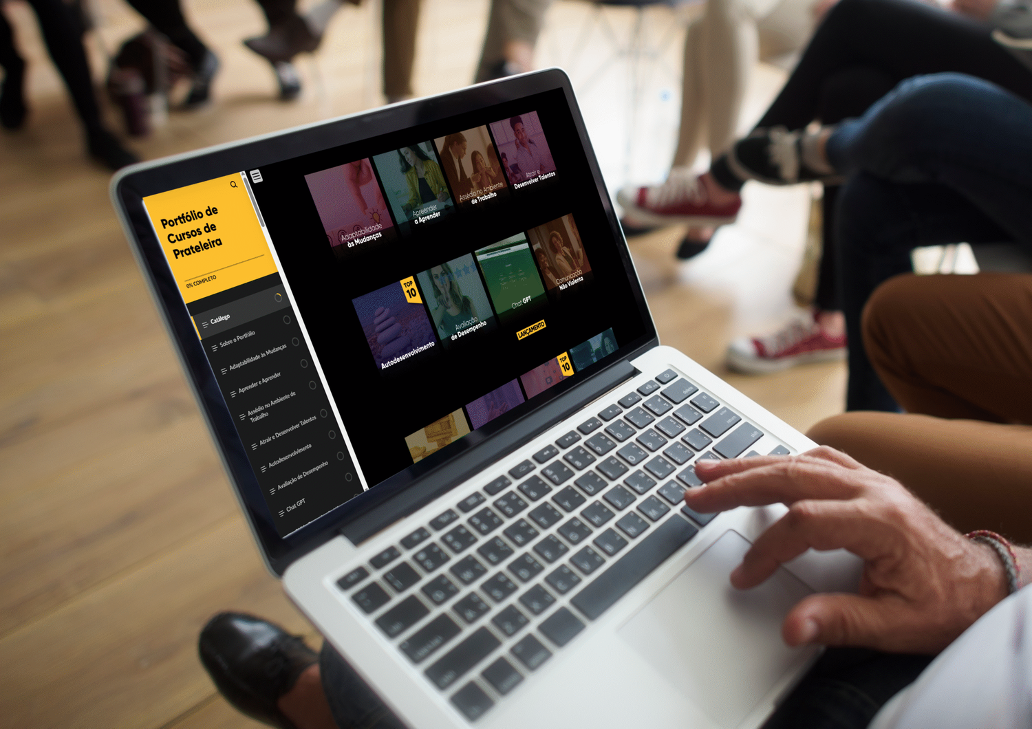 Pessoa usando um laptop exibindo um site com capas de livros. As pessoas ao fundo estão desfocadas.