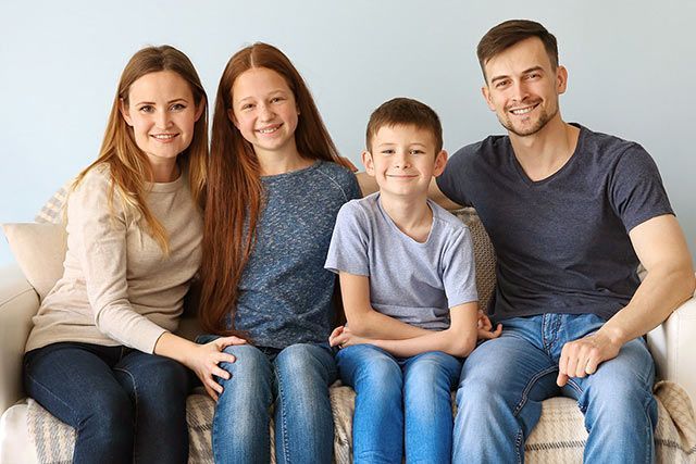 Four people sitting on a couch, smiling in a bright living room.