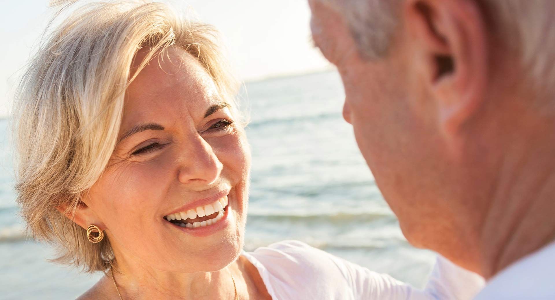 Smiling woman talking with a man by the ocean at sunset